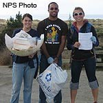 Three Beach Cleanup Volunteers holding litter collected from a beach.