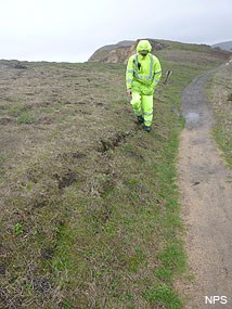 Photo of a park employee standing over and pointing at a newly developed fissure along the Chimney Rock Trail on December 21, 2015. (Click here to download a higher resolution image of this photograph.)