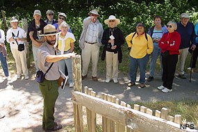 Over ten visitors stand along a pathway while a ranger gestures toward a wooden fence.
