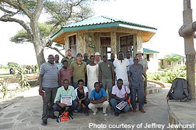 Eighteen people pose in front of a small reception building in Tanzania, Africa.
