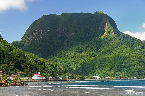 Rainmaker Mountain, a green steep-walled mountain with a bay and buildings in the foreground.