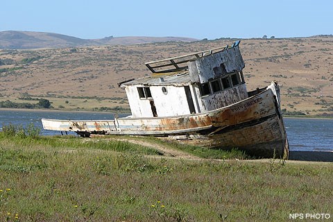 A derelict fishing boat on the edge of Tomales Bay with Bolinas Ridge in the background.