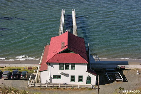 A two-story structure with white walls and a red roof and a dock stretching out into water.