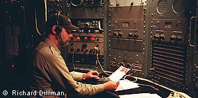 A bearded man wearing a ball cap sits at an old radio transmitting station.