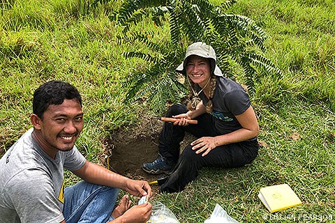 A woman and a man sitting on the ground. The woman holds a digging implement and has her feet in a small hole.