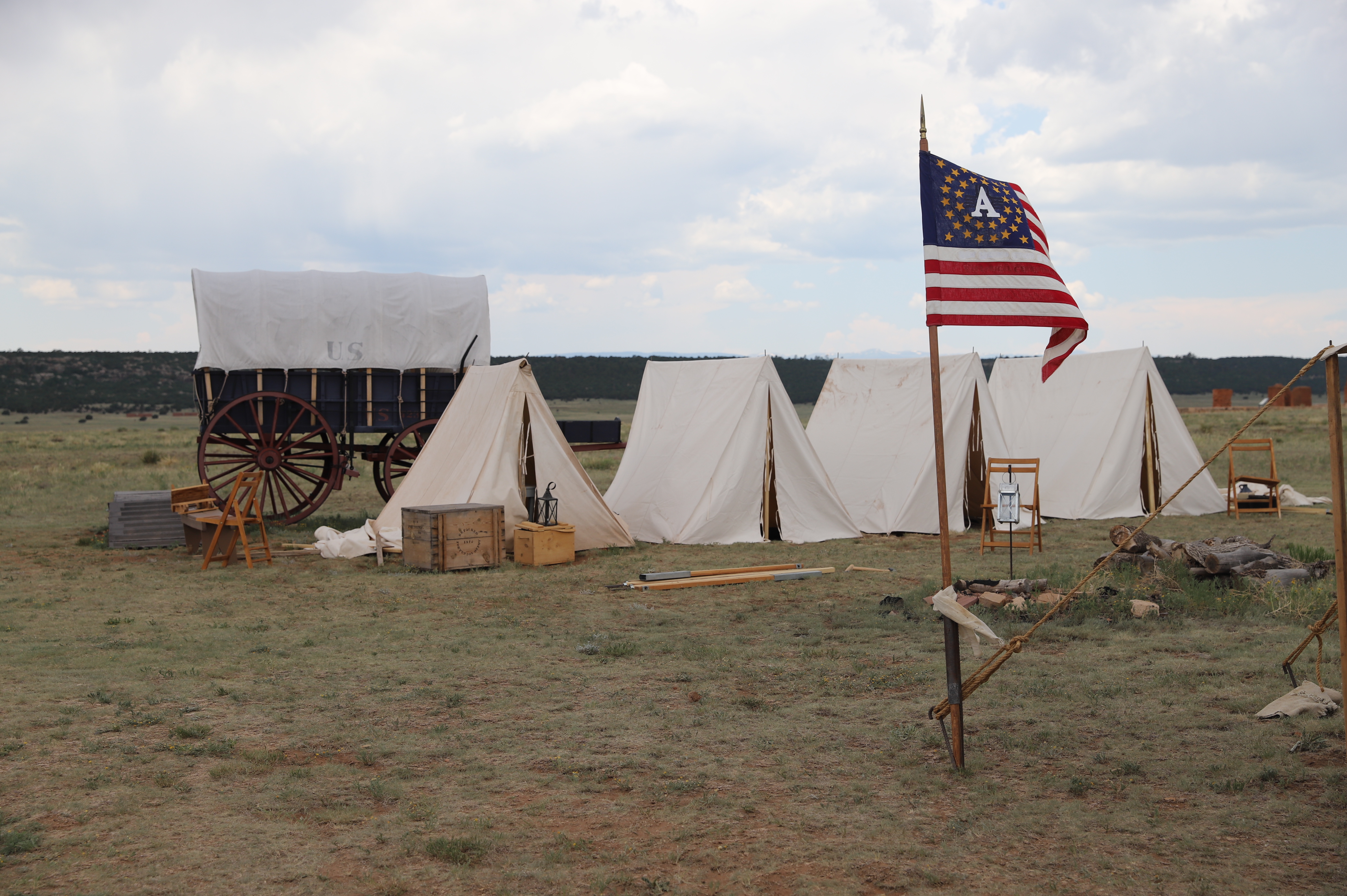 Modern image of tan 1800s style tents with a covered wagon and flag under a mostly cloudy sky.