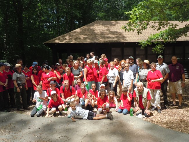a large group of people, many wearing red shirts, pose completing after a service project