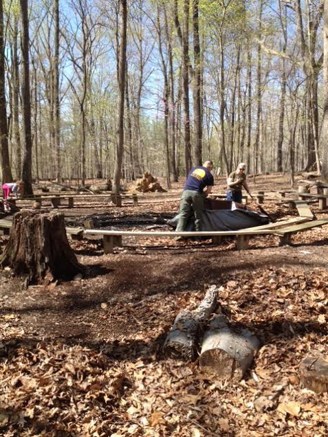 A man, woman, and child clean up a fire pit at a council ring inside Cabin Camp 4. A man, woman, and child clean up a fire pit at a council ring inside Cabin Camp 4.