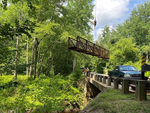 Metal footbridge dangle from a crane near a roadway in the forest