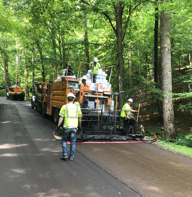 Construction workers operate heavy equipment on road in Prince William Forest Park as part of pavement sealing and paving project.