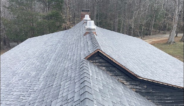 New slate grey roof shakes cover the top of a large wooden building in a winter forest