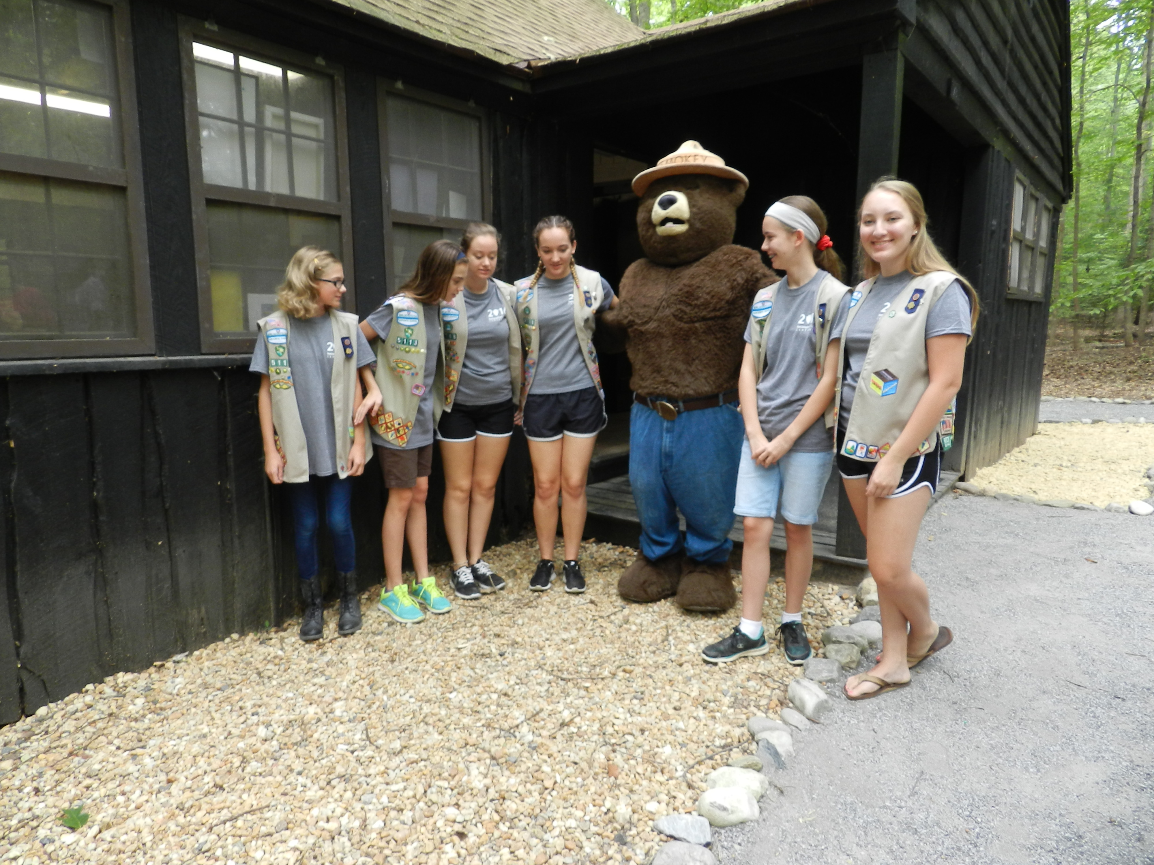 A group of girl scouts wearing scouting vests meet Smokey Bear at the Craft Cabin