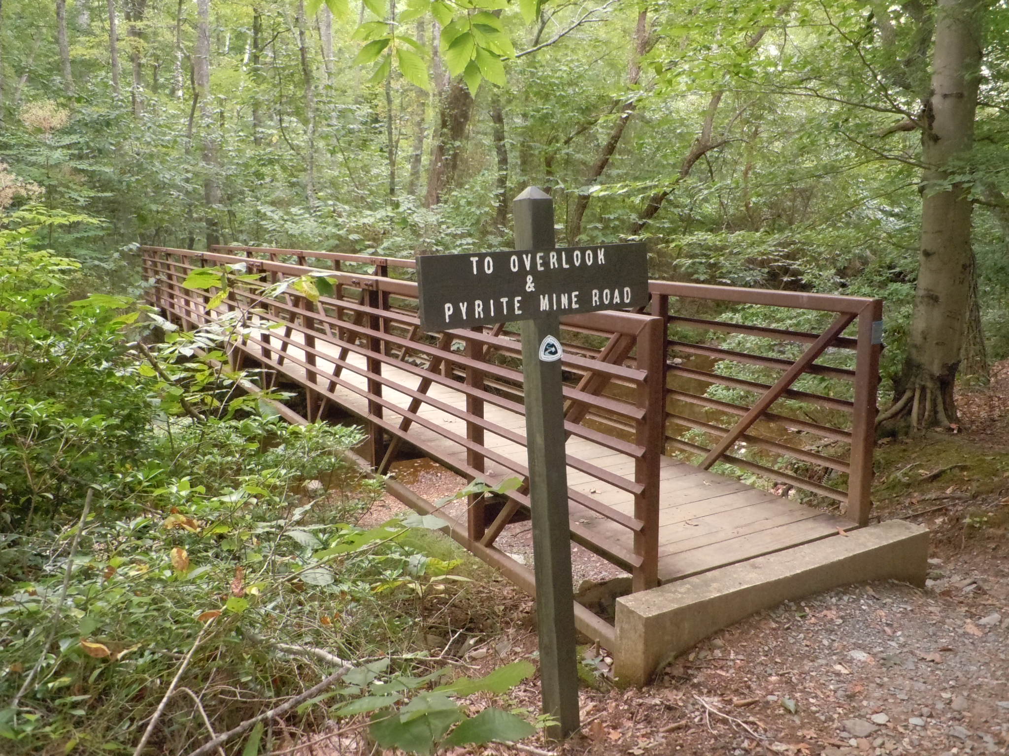 a wood and metal pedestrian bridge scans a creek in summer