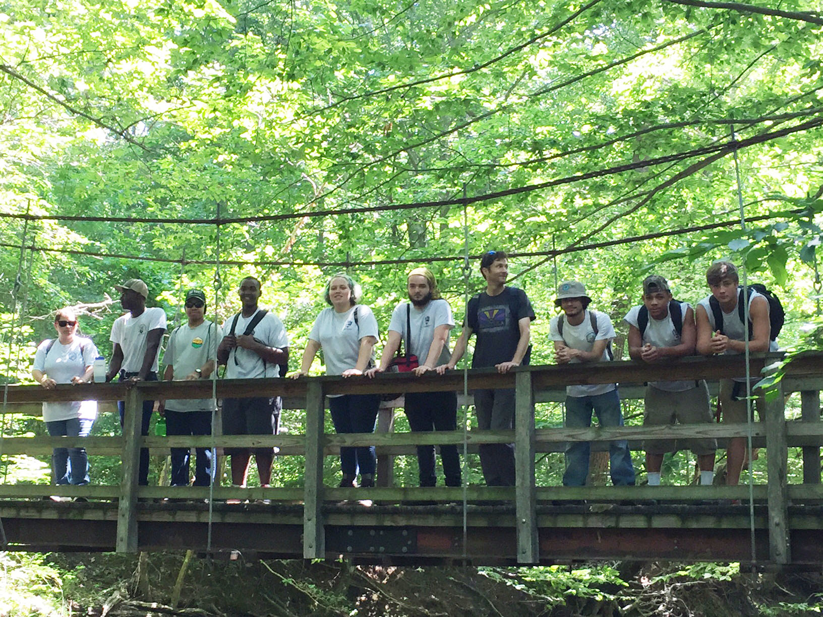 Nine YCC members and a leader stand on a bridge over the Quantico Creek.