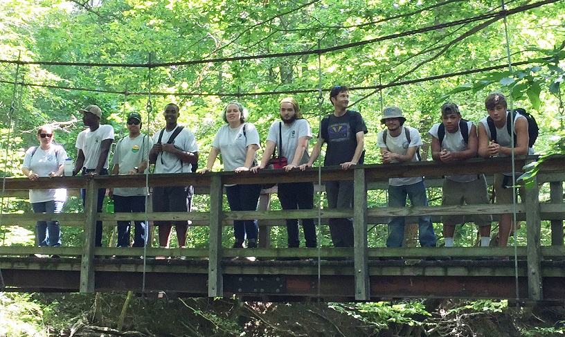 10 high school students standing and leaning on a suspension bridge in the forest