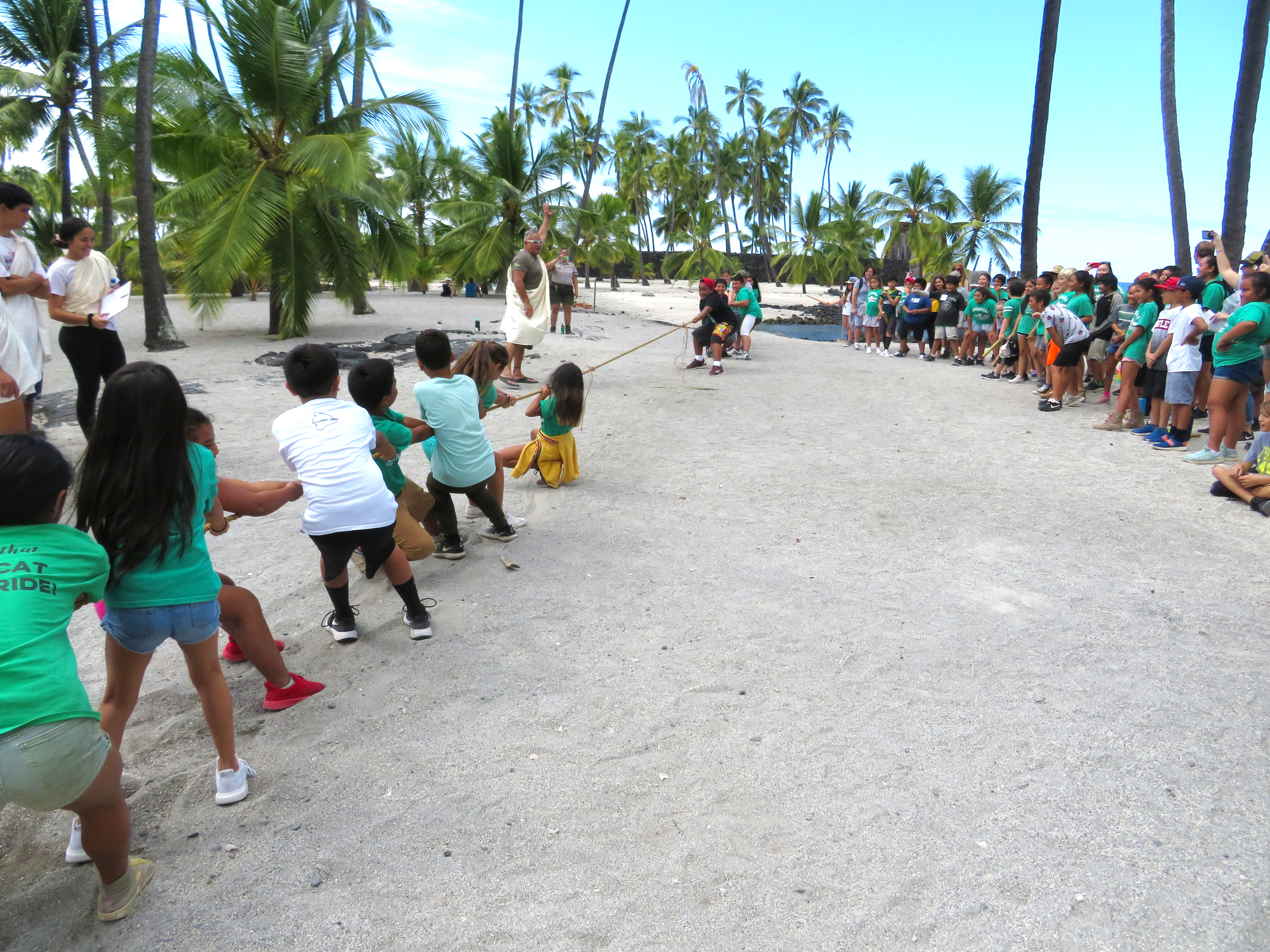 School children play huki huki (tug of war) upon the sandy shores of the Royal Grounds. A referee in a white kihei signals the start of the game.