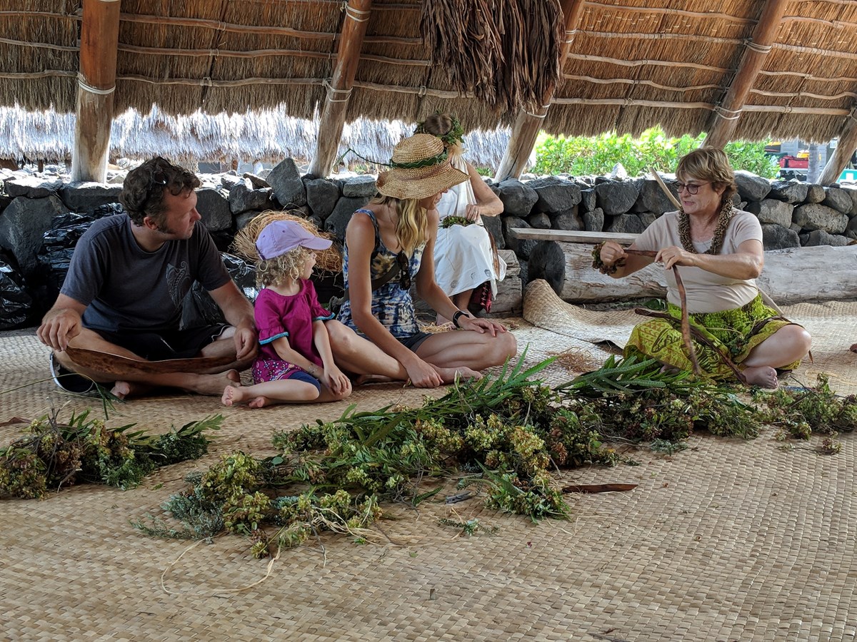 A family of four learns how to make a lei from a cultural demonstrator.