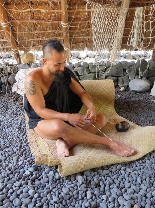 Man in traditional clothing demonstrates traditional rope-making techniques.
