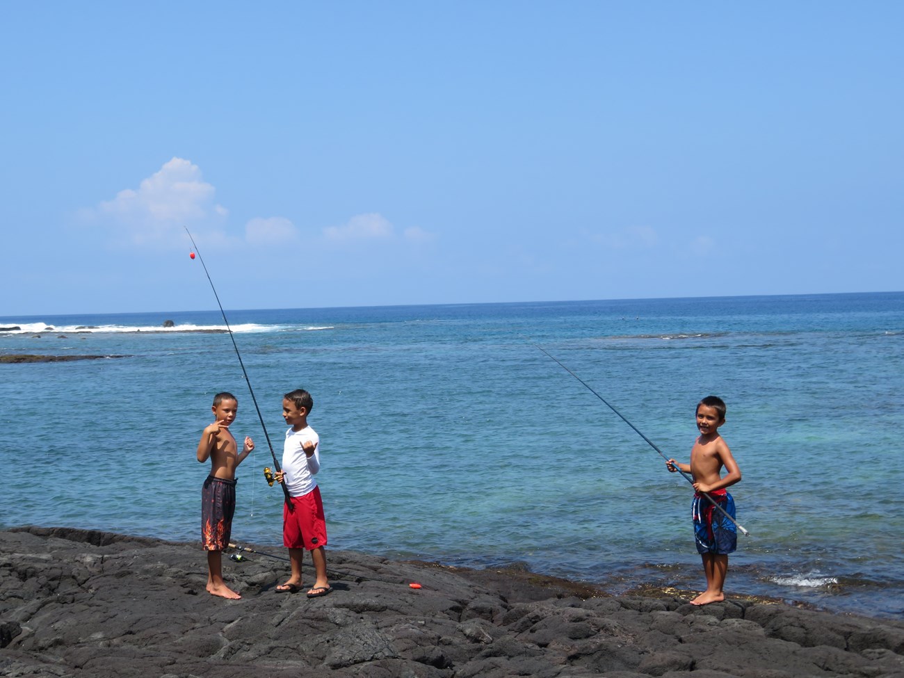 Three children pose with their fishing poles by the ocean.