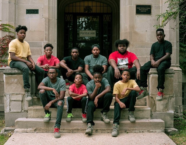 Ten African American boys sit on the grey stone steps of a building with neutral expressions.