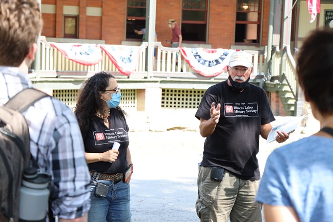 A woman and man stand in front a tour group wearing shirts that say Illinois Labor History Society.