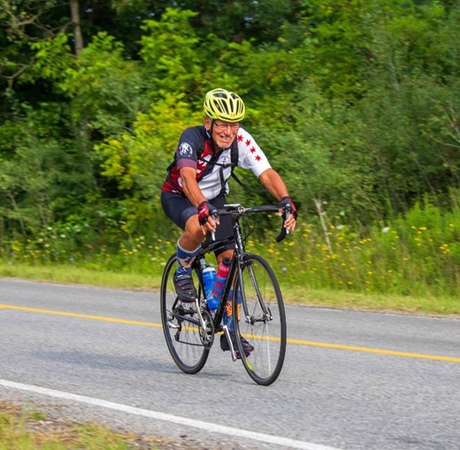 Ron on bike A man rides a bicycle on a trail wearing a green helmet and a Chicago flag themed bike jersey.