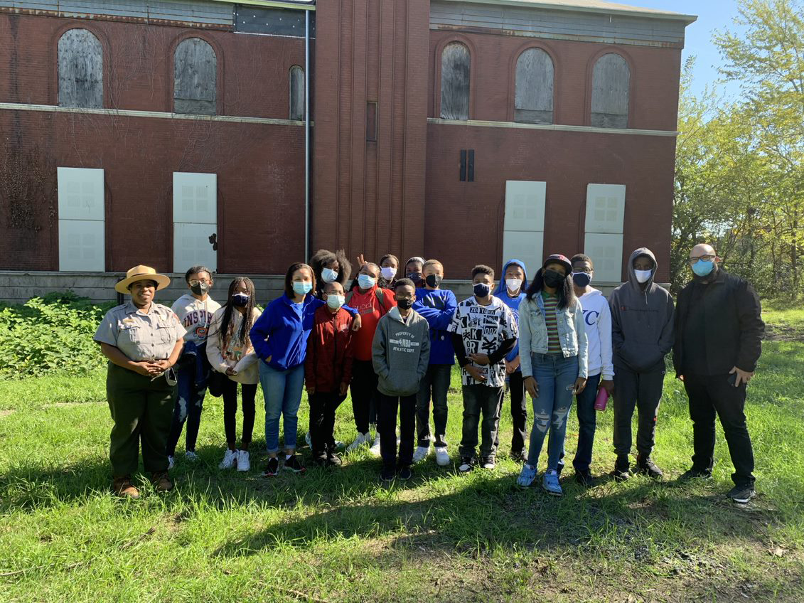 rangerveamberandpoestudents A group of students, two teachers, and a ranger pose with masks on in front of a historic brick building.