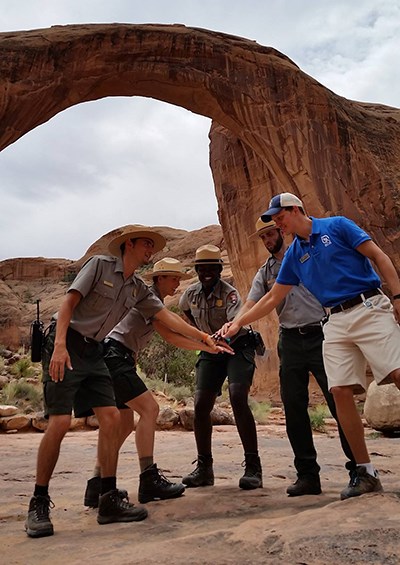 Group of rangers and boat tour guide huddle in front of Rainbow Bridge