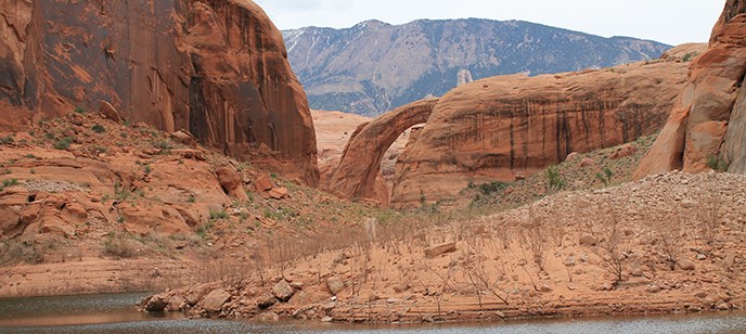 Rainbow Bridge. Navajo Mountain in the background. Water in the foreground.