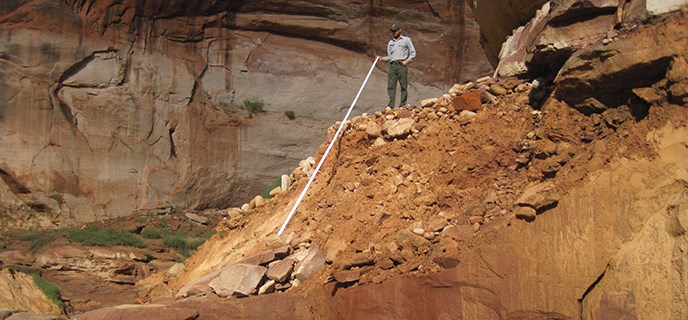 Park Ranger stands on top of a sandy landslide holding a measuring stick to the bottom. Park Ranger stands on top of a sandy landslide holding a measuring stick to the bottom.