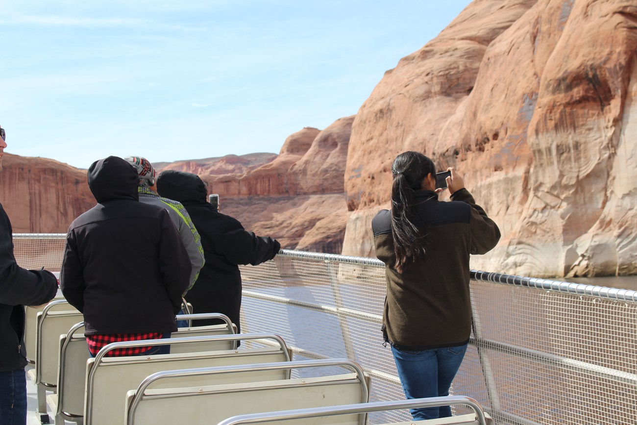 Person takes photos with phone while on viewing deck of boat weaving through canyon
