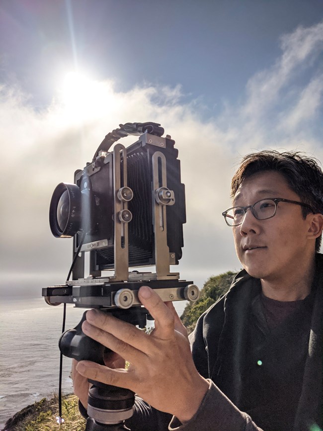 Bobby Lee adjusting a camera outdoors.