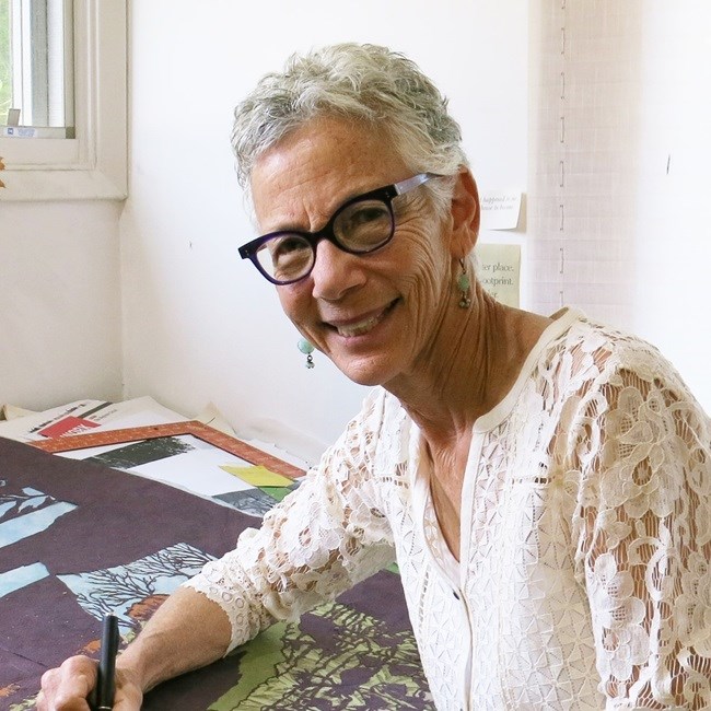 A woman with short white hair and a white shirt smiling while working on papercut art.
