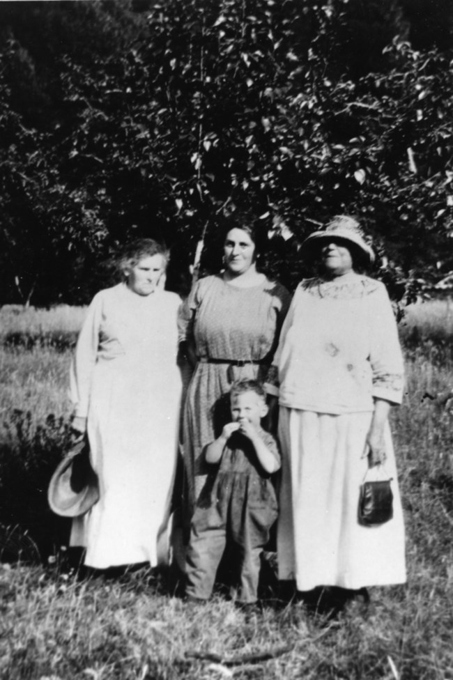 Black and white image of family of four stand in an orchard.