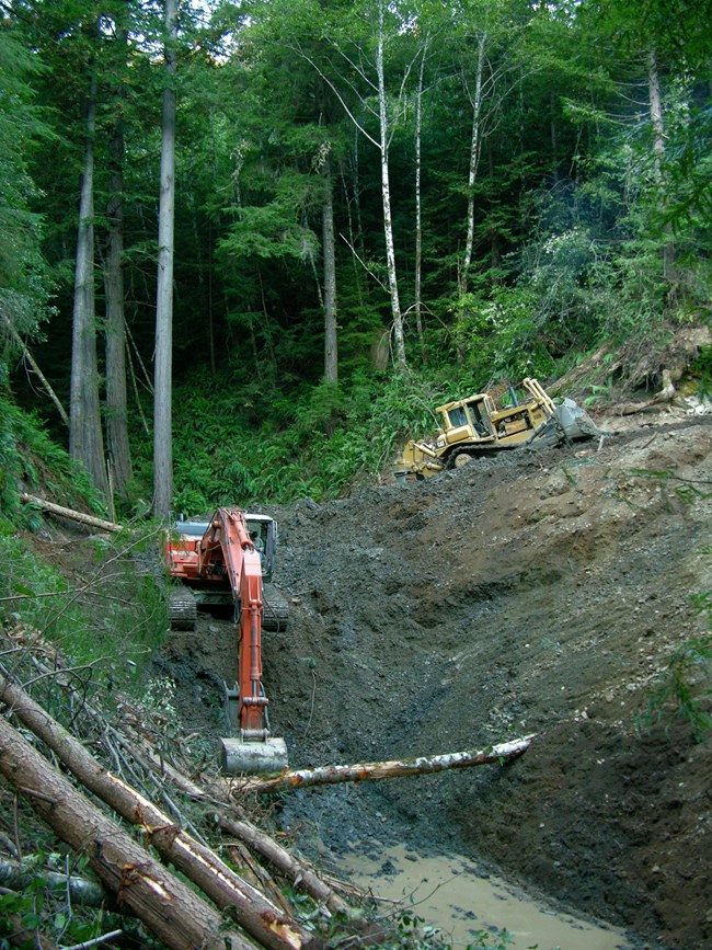 Large machinery removes dirt to reveal a natural stream bed.