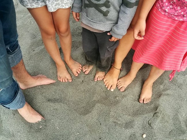Children's feet on a grey sandy beach.