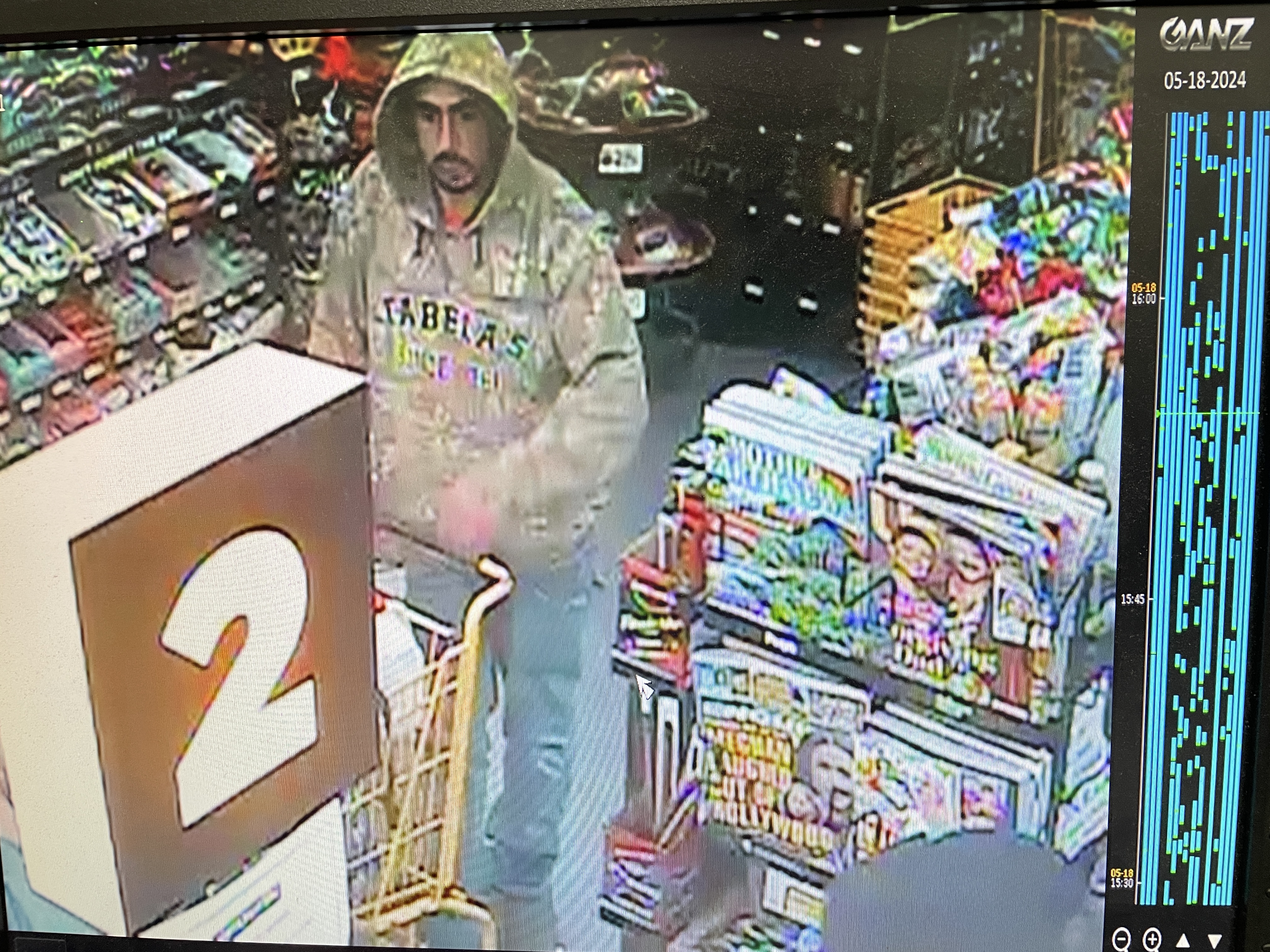 A man with a dark mustache inside a store. He is wearing jeans and a brown hoodie with the work "Cabela's"