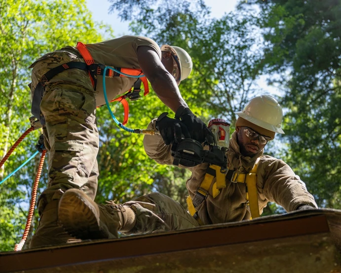 Two Air Force members using a power tool to repair a roof.