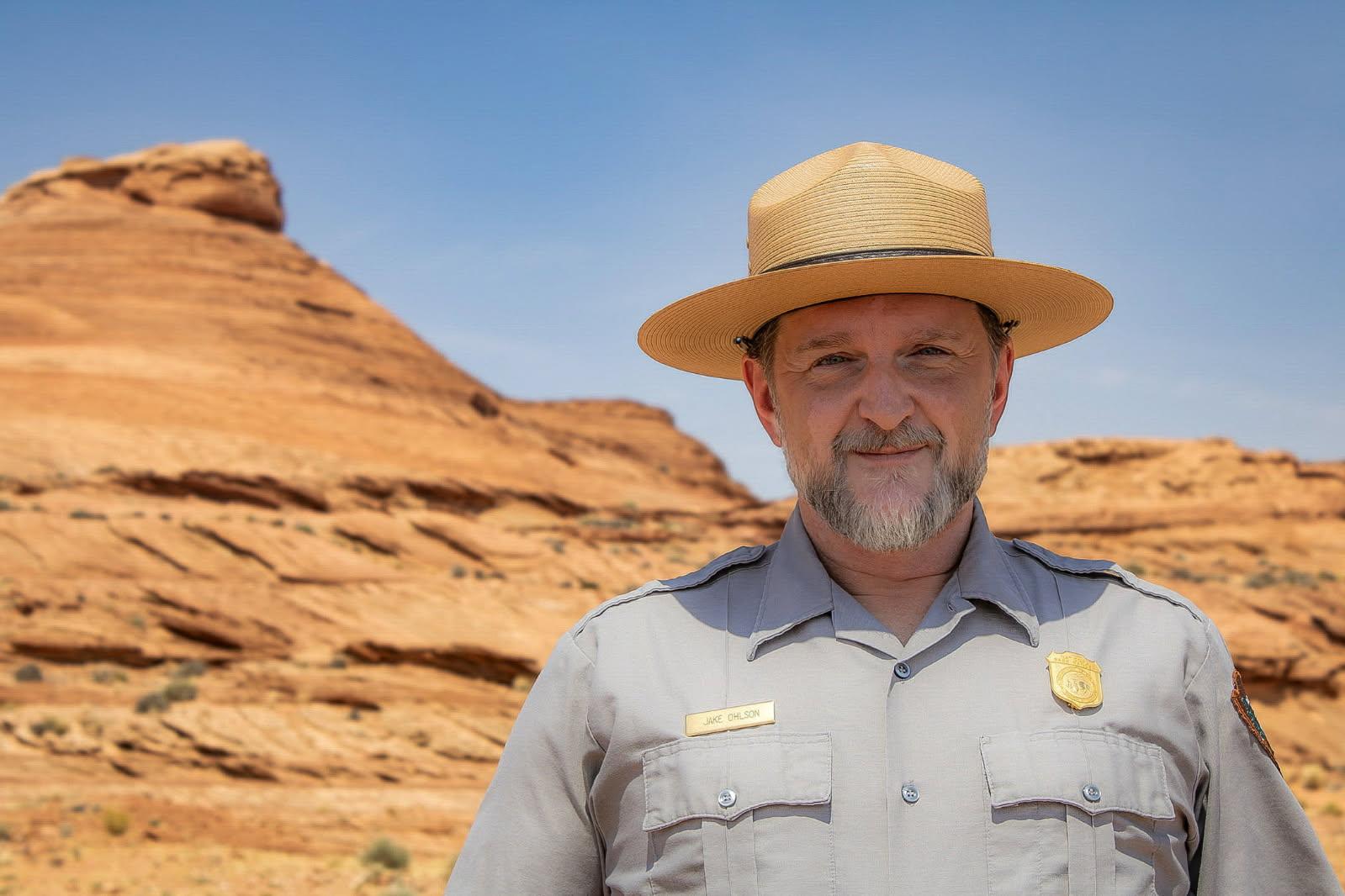 Ranger Jake Ohlson in uniform standing outside on a sunny day with a rocky landscape behind him,