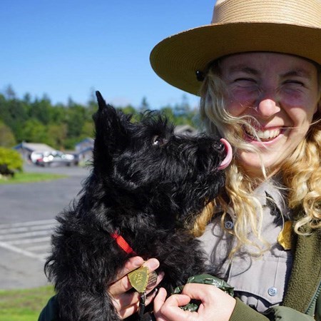 A black dog licks a park ranger.