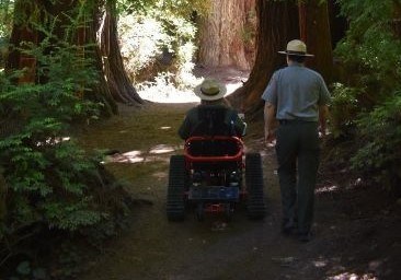 Park ranger rides in a red all-terrain wheeled track chair on a trail through the forest