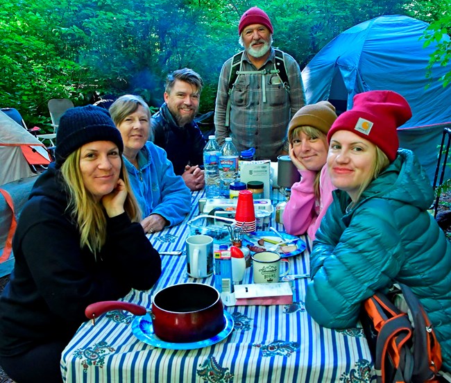 Family of six gather around a campground picnic table