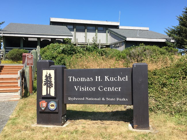 A brown and gray building, with steps and a wooden sign.