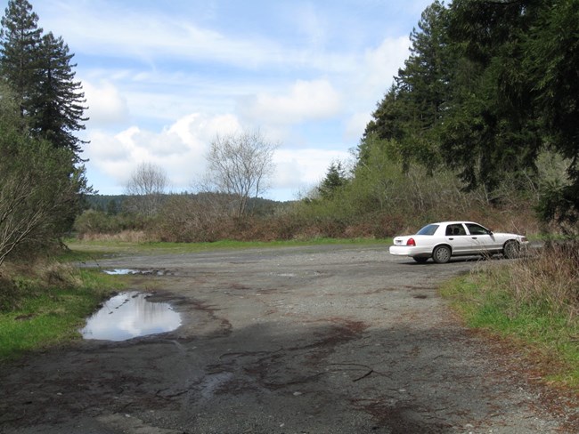 Open gravel parking lot with one car parked to the right