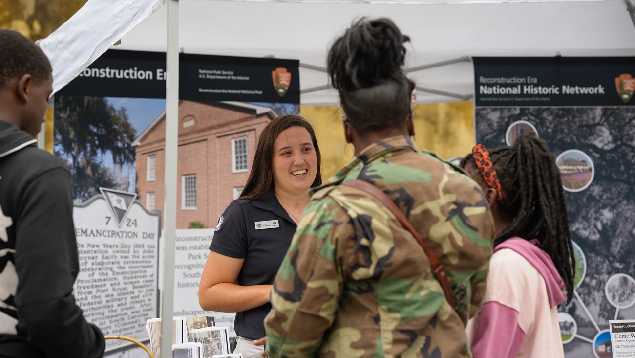 A woman talks to a group of people at a tent about Reconstruction Era National Historical Park.