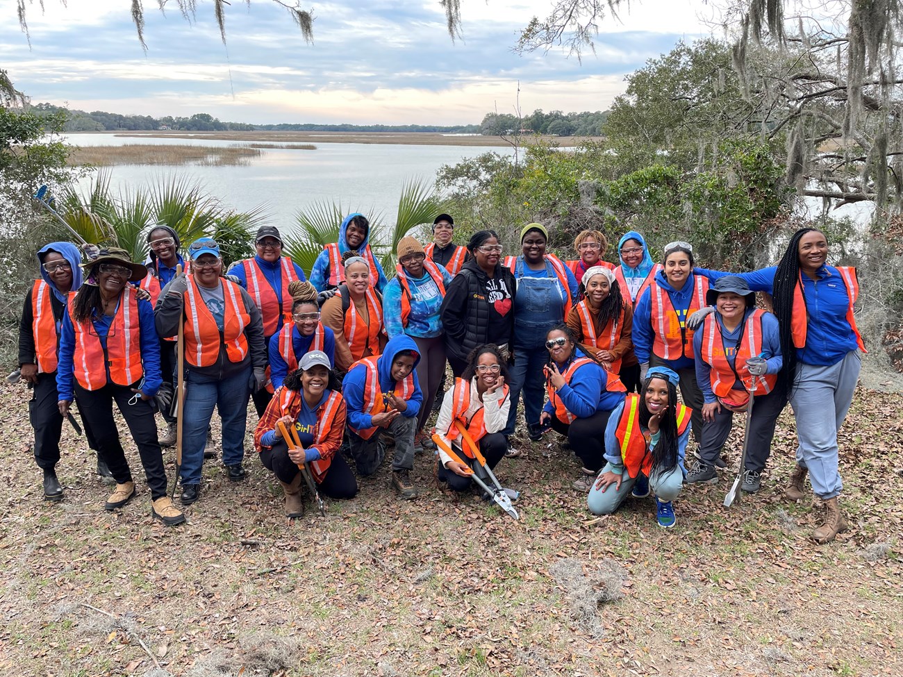 A group of women in PPE with trail equipment stand in front of a marshy area.