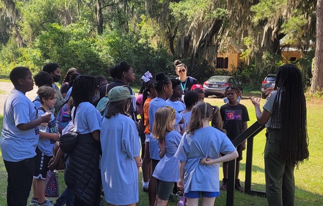 A park ranger talks to a group of young people around an outdoor exhibit sign.