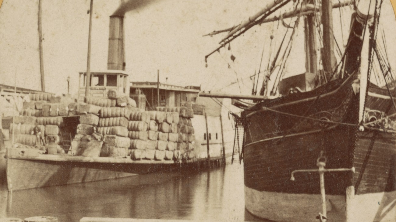 A steam ship sits in a harbor loaded with bales of goods.