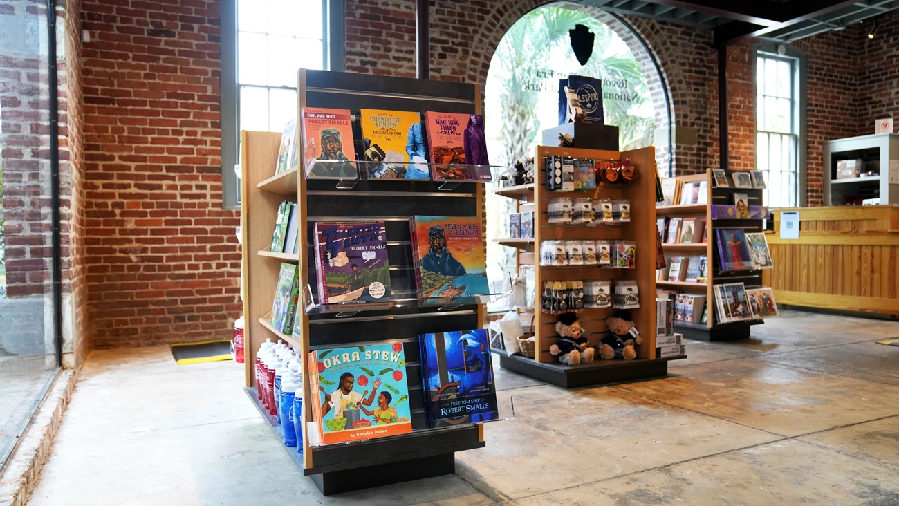 Reconstruction Era National Historical Park Bookstore A small bookstore with three shelves of books and trinkets laid out in front of a three windows and a desk.