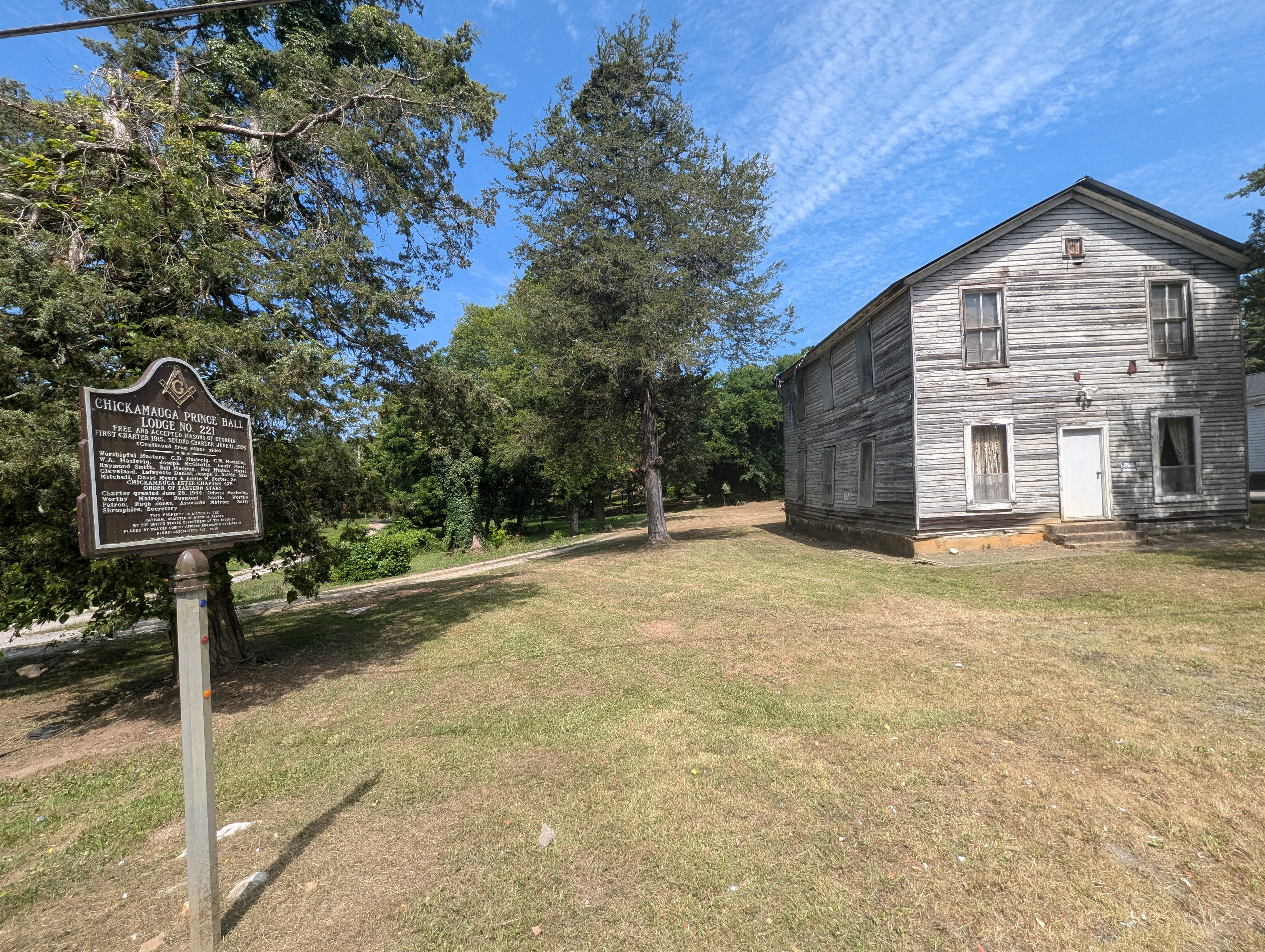 Old Wooden Building that resembles an unpainted barn. There is a state historic marker in the foreground.